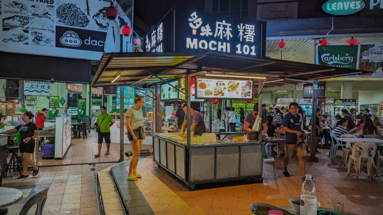 A landscape picture of Andrea from Whaling Around ordering some mochi at a Malaysian food court in Kuching Malaysia